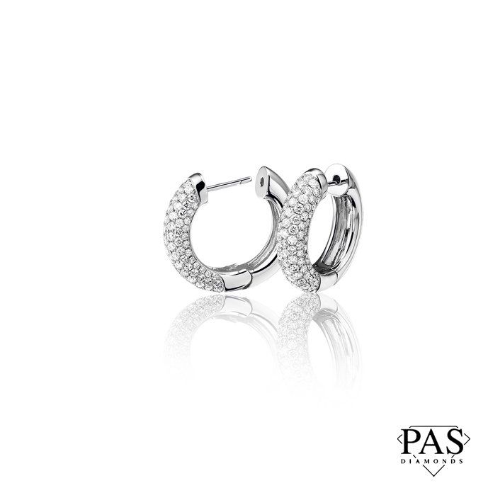 Oorbellen van witgoud met kleine diamantjes, weerspiegeld op een wit oppervlak.