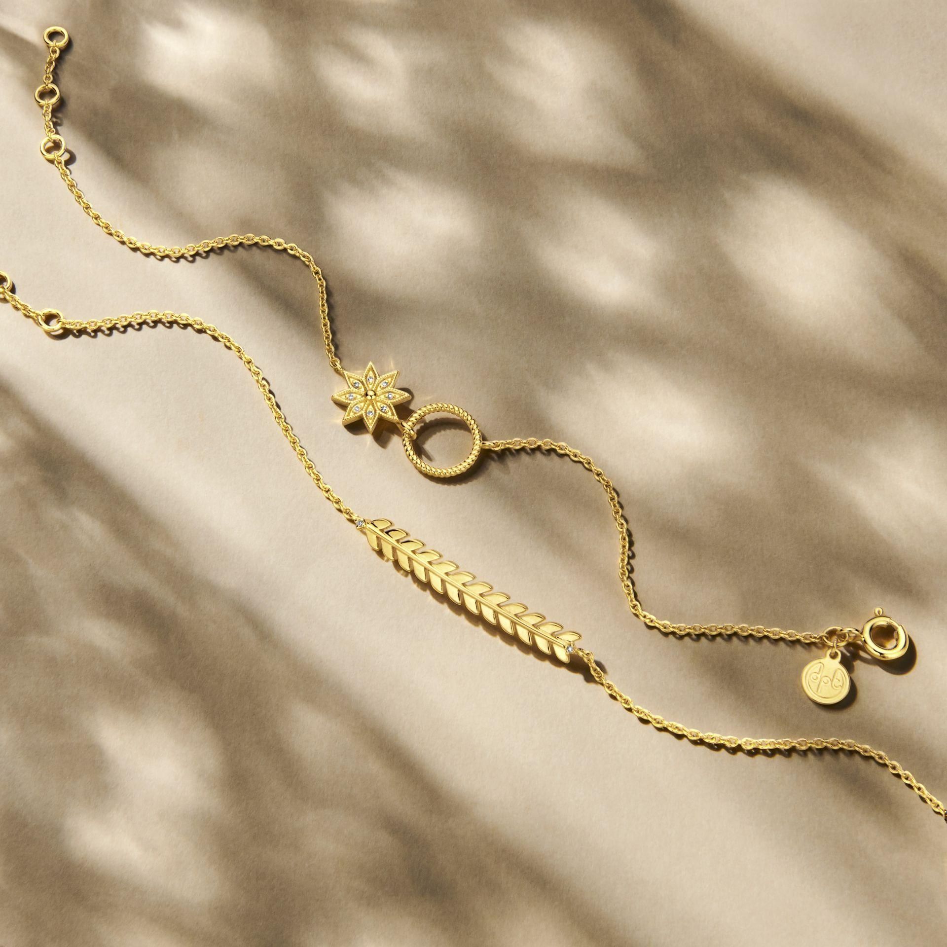 Twee delicate gouden armbanden op een gestructureerde achtergrond; één met een sterpatroon en één met een bladmotief.