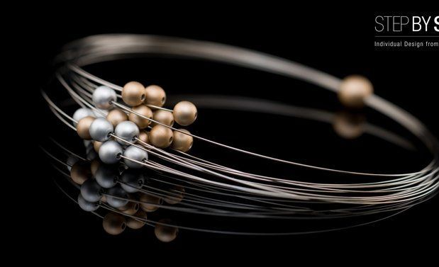 Armband van zilver en gouddraad met reflecterende zwarte achtergrond. Gouden en zilveren kralen zijn op één punt geclusterd.