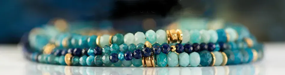 Armbanden in verschillende tinten blauw en goud liggen op een wit oppervlak met een wazig blauwe achtergrond.