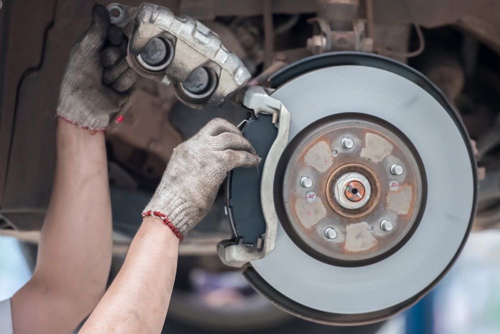 A Person Is Fixing a Brake Pad on A Car — Currajong Brake Parts Pty Ltd In Currajong, QLD