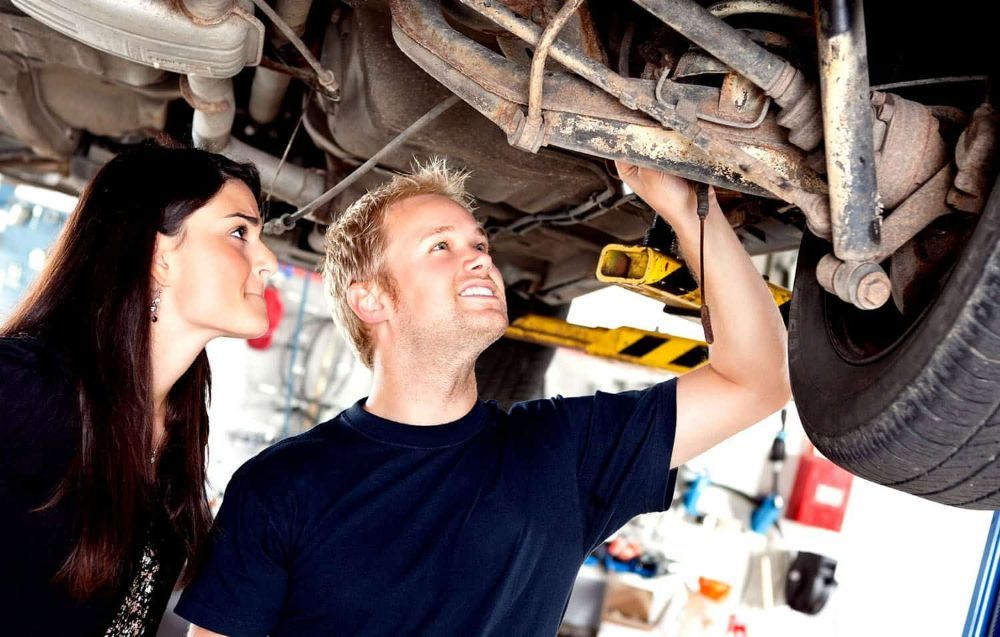 A Man and A Woman Are Looking Under a Car in A Garage — Currajong Brake Parts Pty Ltd In Currajong, QLD