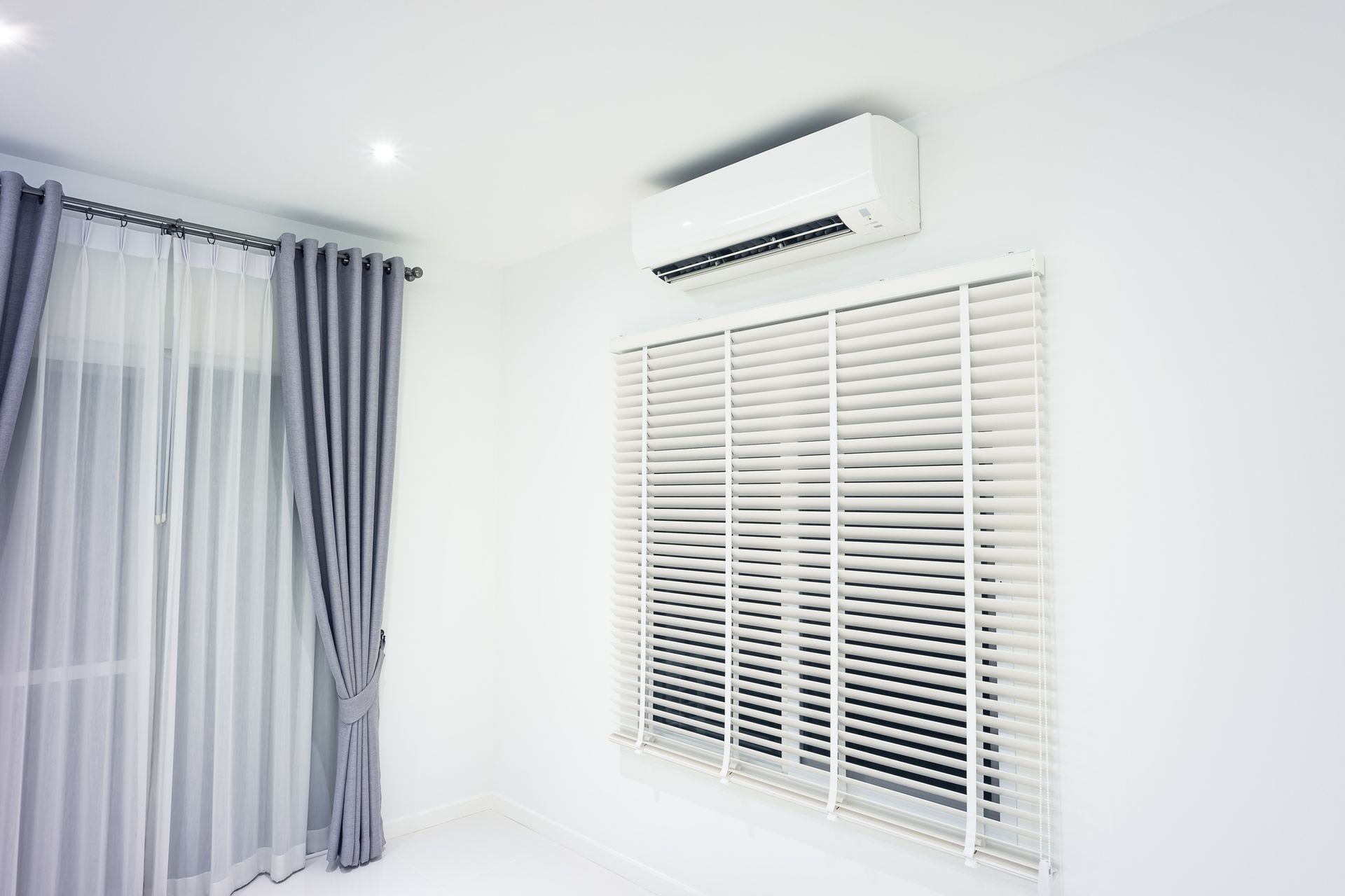 White room with AC unit above a window with blinds, gray curtains.