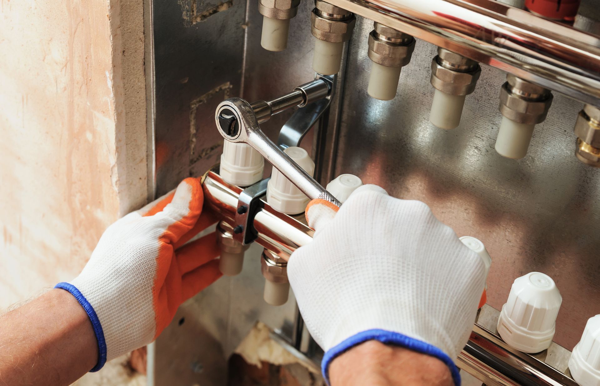 Hands in gloves using a wrench on plumbing pipes, close up.