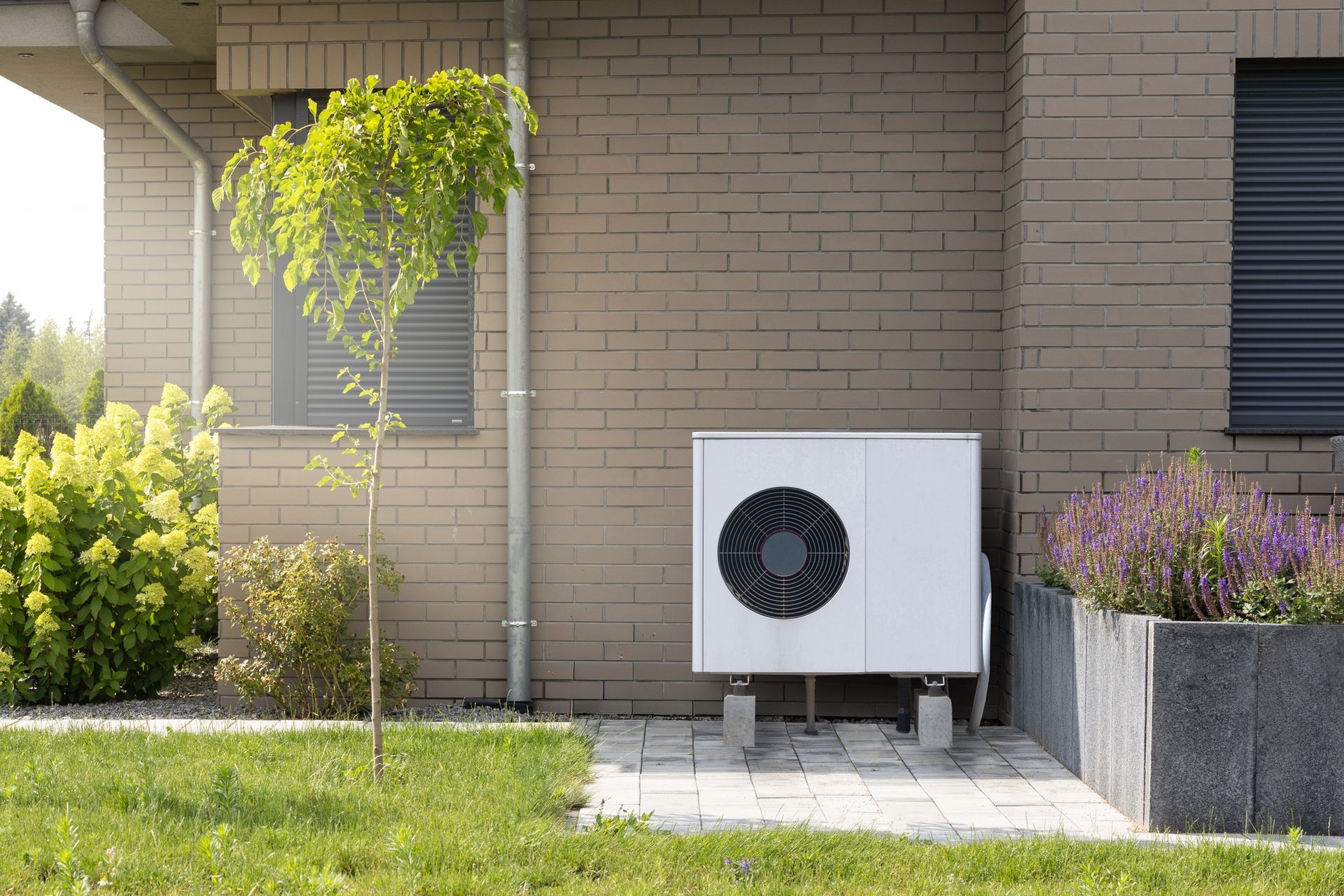 Air source heat pump unit mounted on concrete next to brick house.