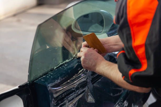 A Man Is Applying Window Tinting To A Car Window — Waipahu, HI — Leeward Auto Glass