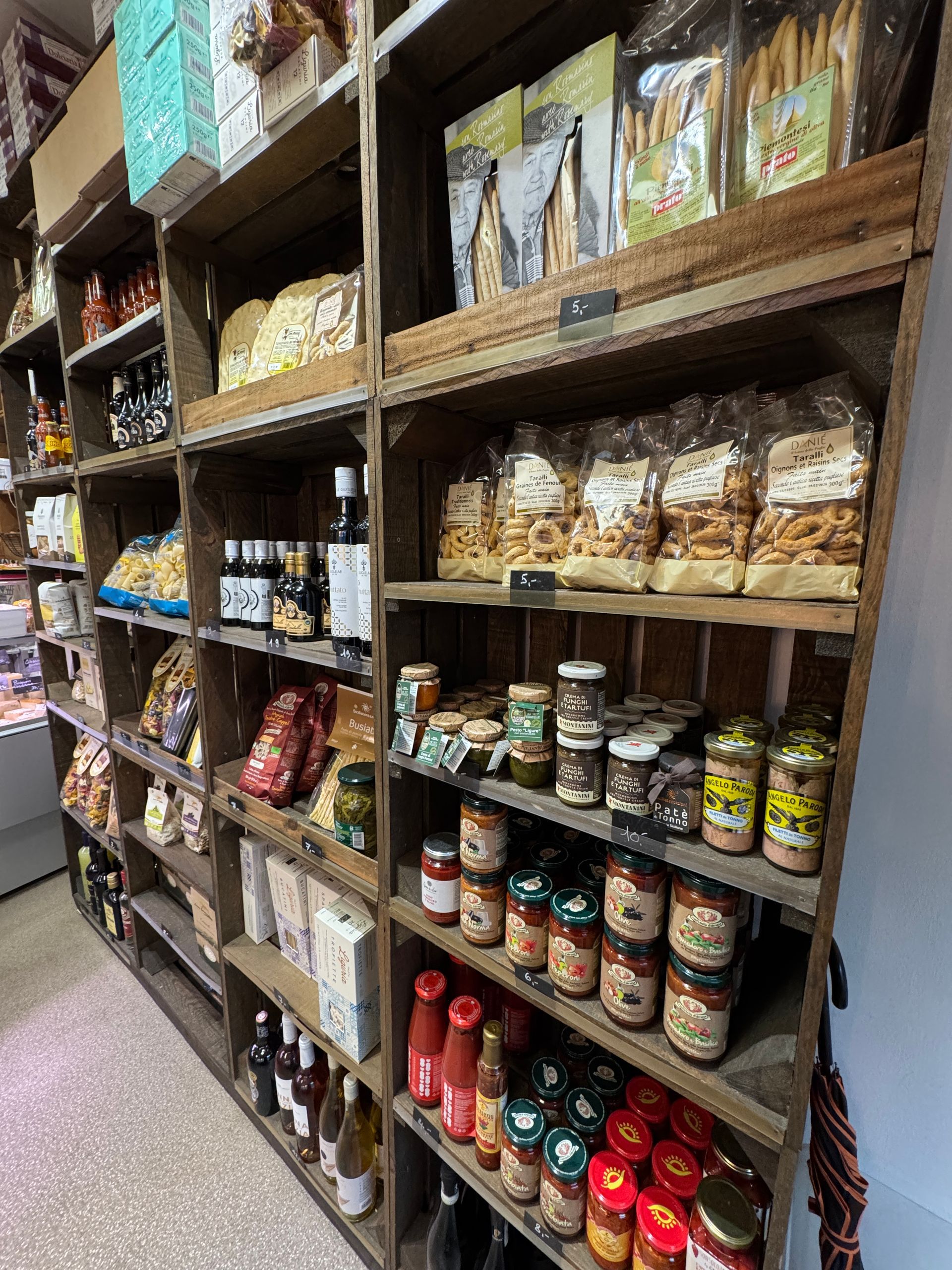 Des étagères en bois garnies de divers produits alimentaires, notamment des bocaux, des bouteilles et des produits emballés, dans un magasin.