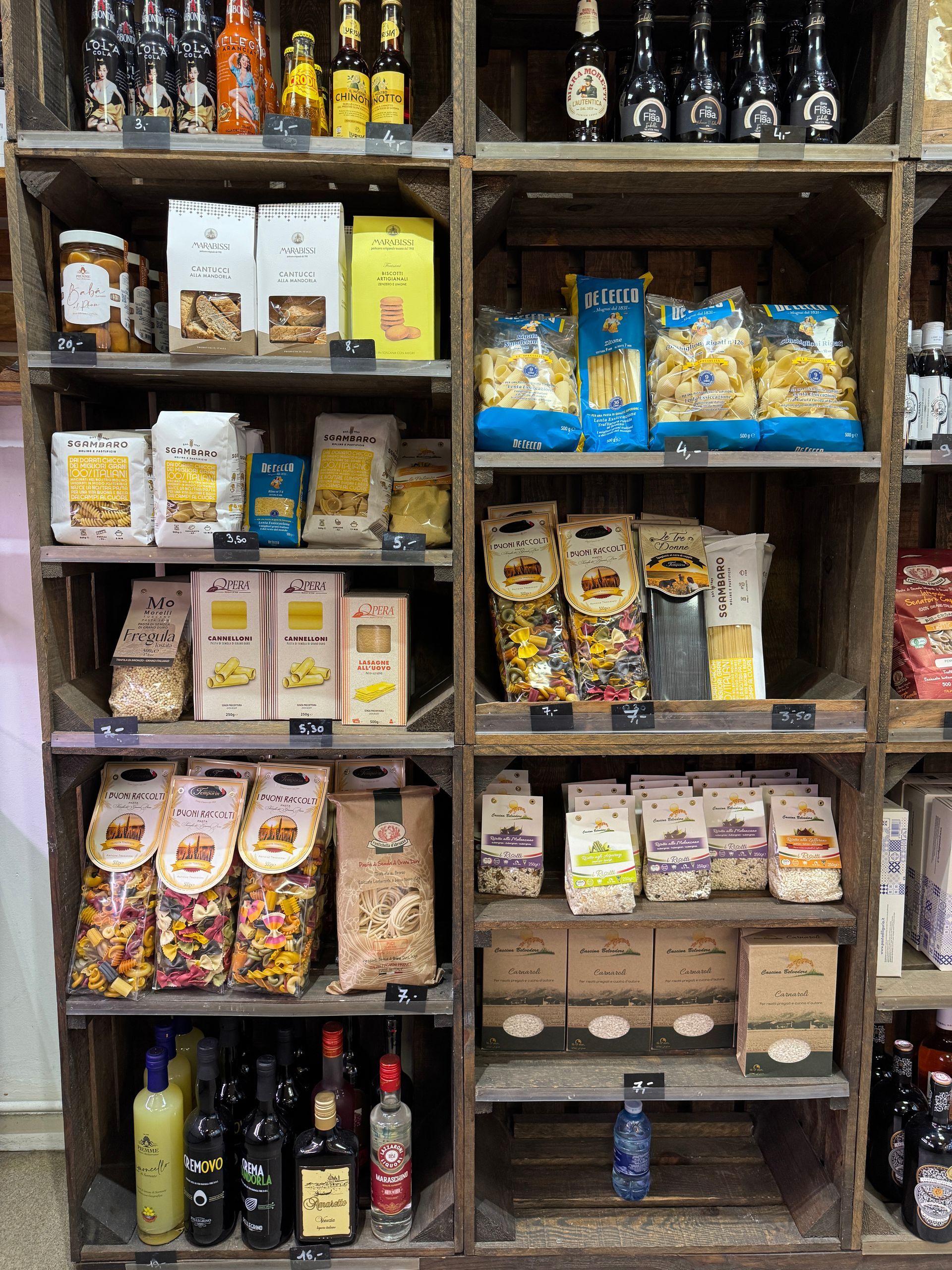 Des étagères présentent des produits alimentaires emballés dans un présentoir en bois. Pâtes, sauces et boissons en bouteille sont disposées pour la vente.