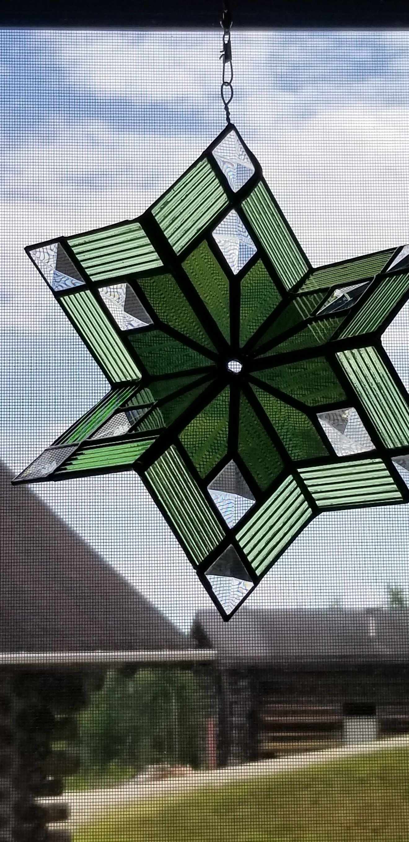 A green stained glass snowflake is hanging from a window.