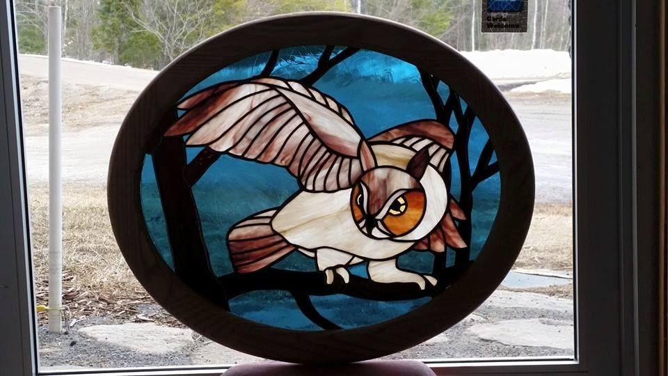 A stained glass owl is sitting on a branch in front of a window.