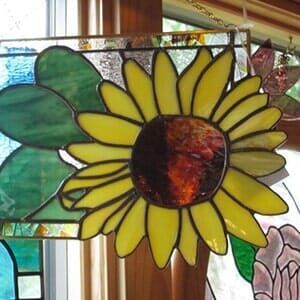 A stained glass sunflower is hanging on a window sill.