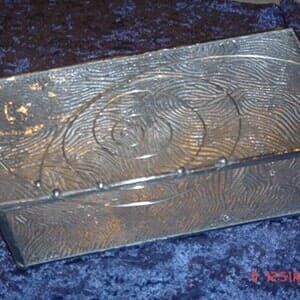 A silver box with a spiral design is sitting on a blue carpet.