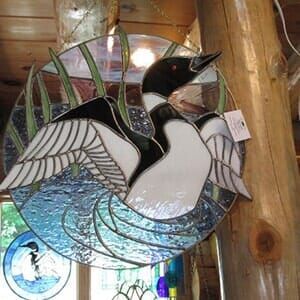 A stained glass window with a duck on it is hanging on a wooden wall.