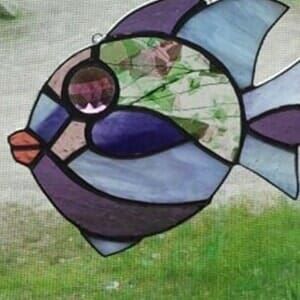 A stained glass fish is hanging on a window.