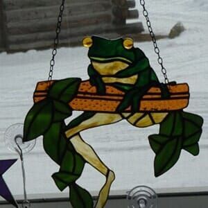 A frog is sitting on a swing with leaves on it.