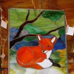 A stained glass painting of a fox laying under a tree branch