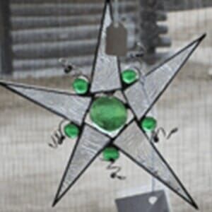 A stained glass star with green beads hanging from a fence