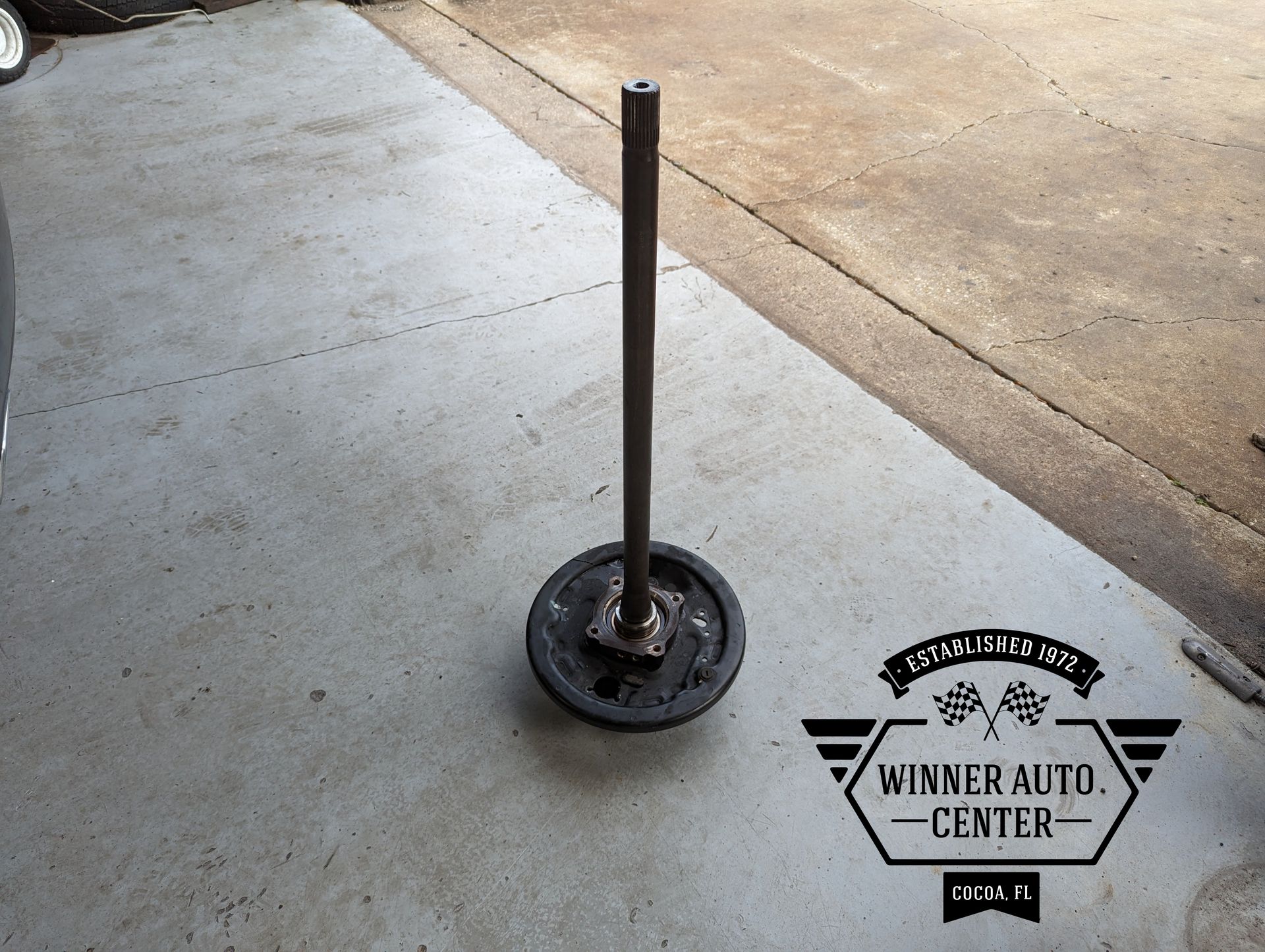 A black, circular car brake drum with a vertical metal rod attached | Winner Auto Center