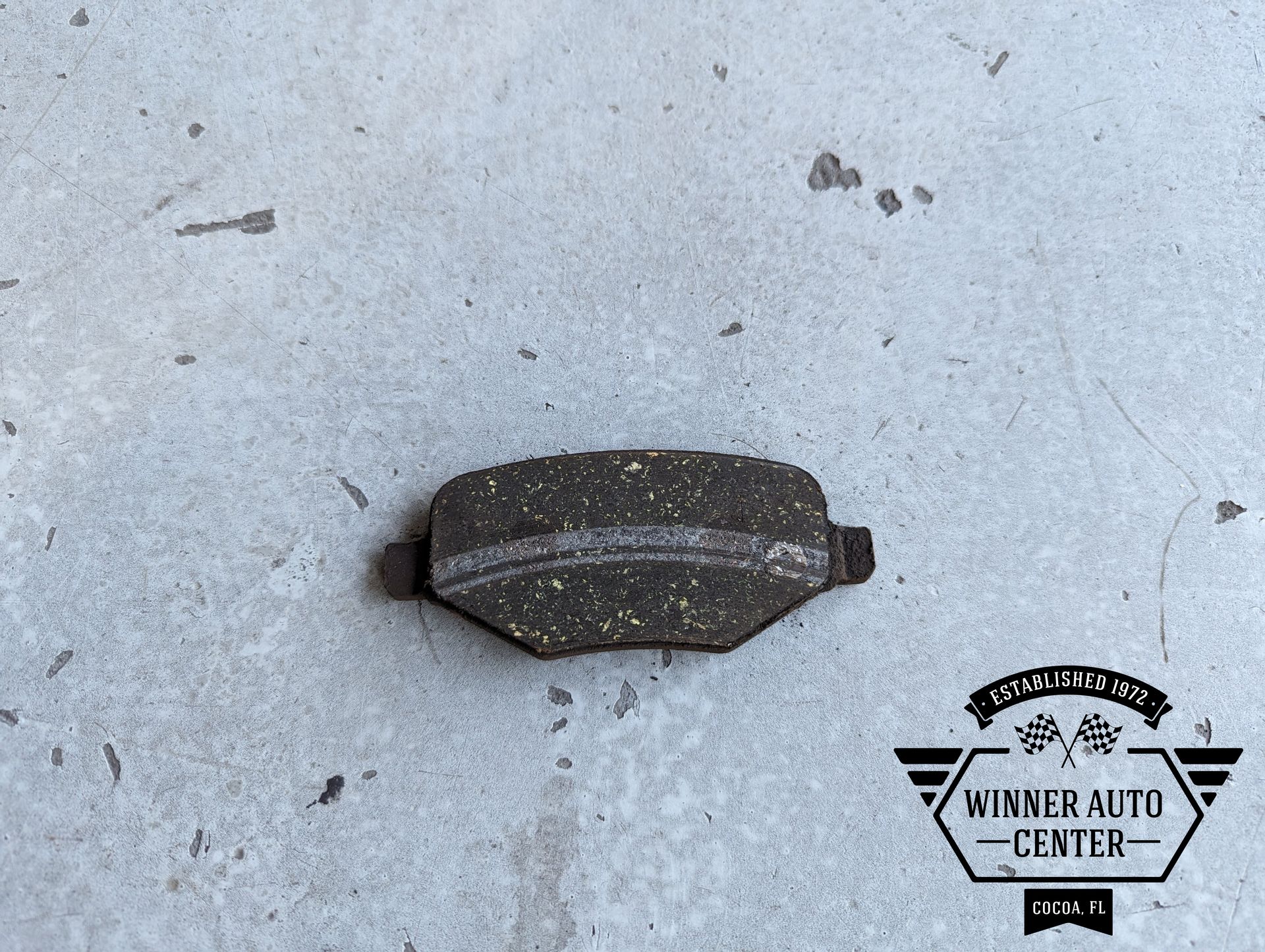 A worn brake pad on a gray concrete surface | Winner Auto Center