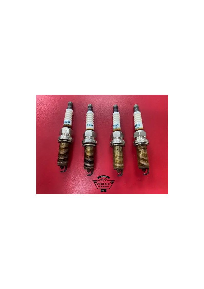 Four used spark plugs on a red surface | Winner Auto Center
