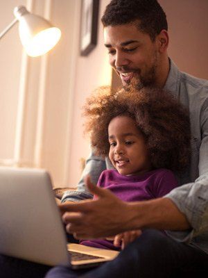 Father and daughter participating in virtual funeral service via laptop.