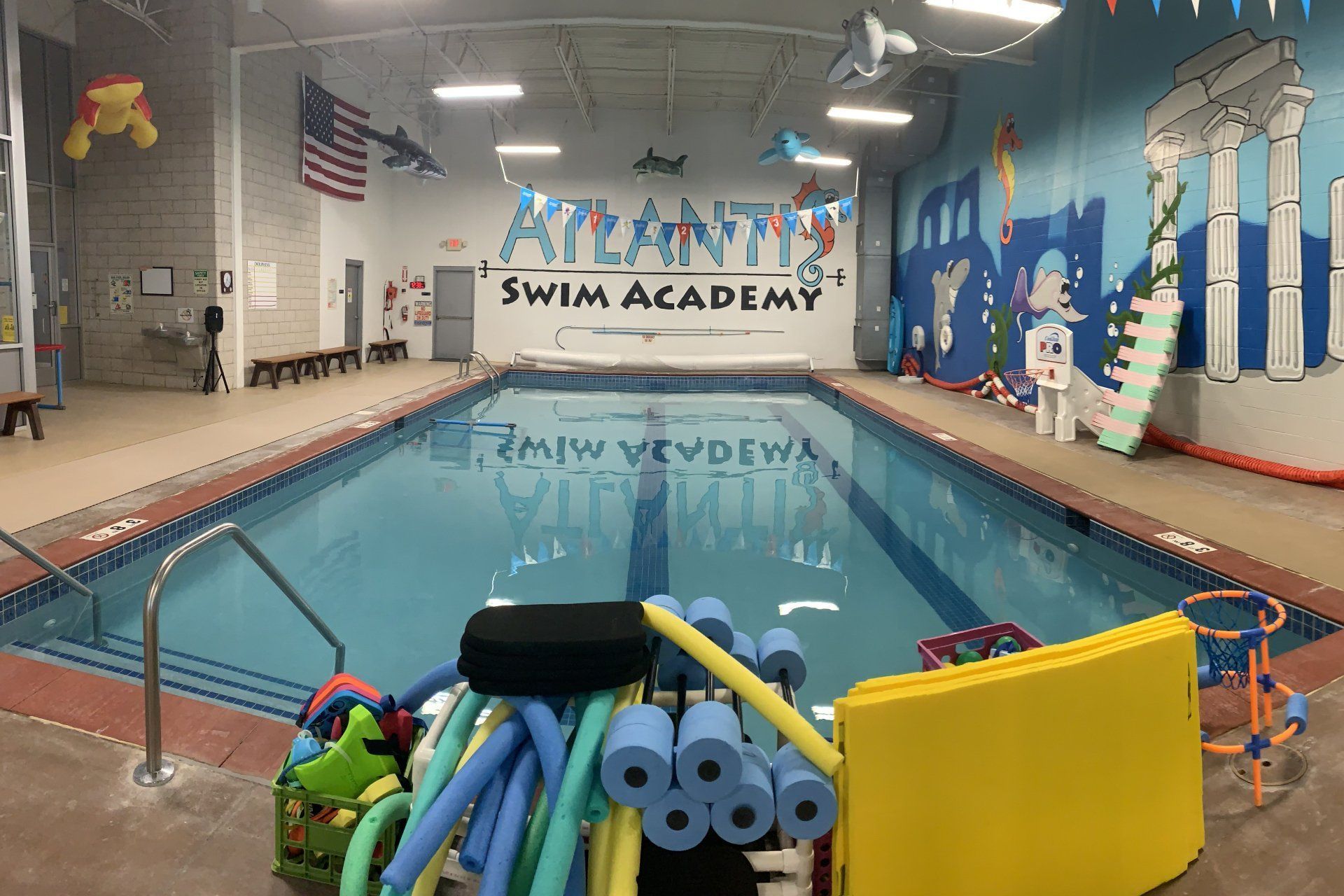 Indoor swimming pool at Atlantis Swim Academy with colorful pool noodles and flotation devices.