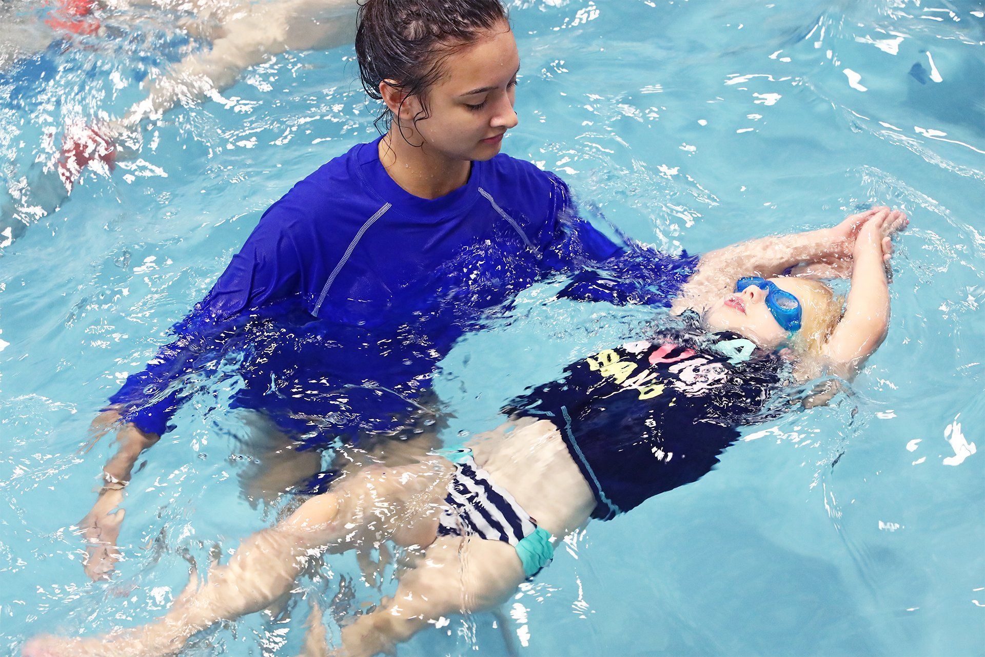 Swimming instructor assisting a child in the water; blue pool setting.