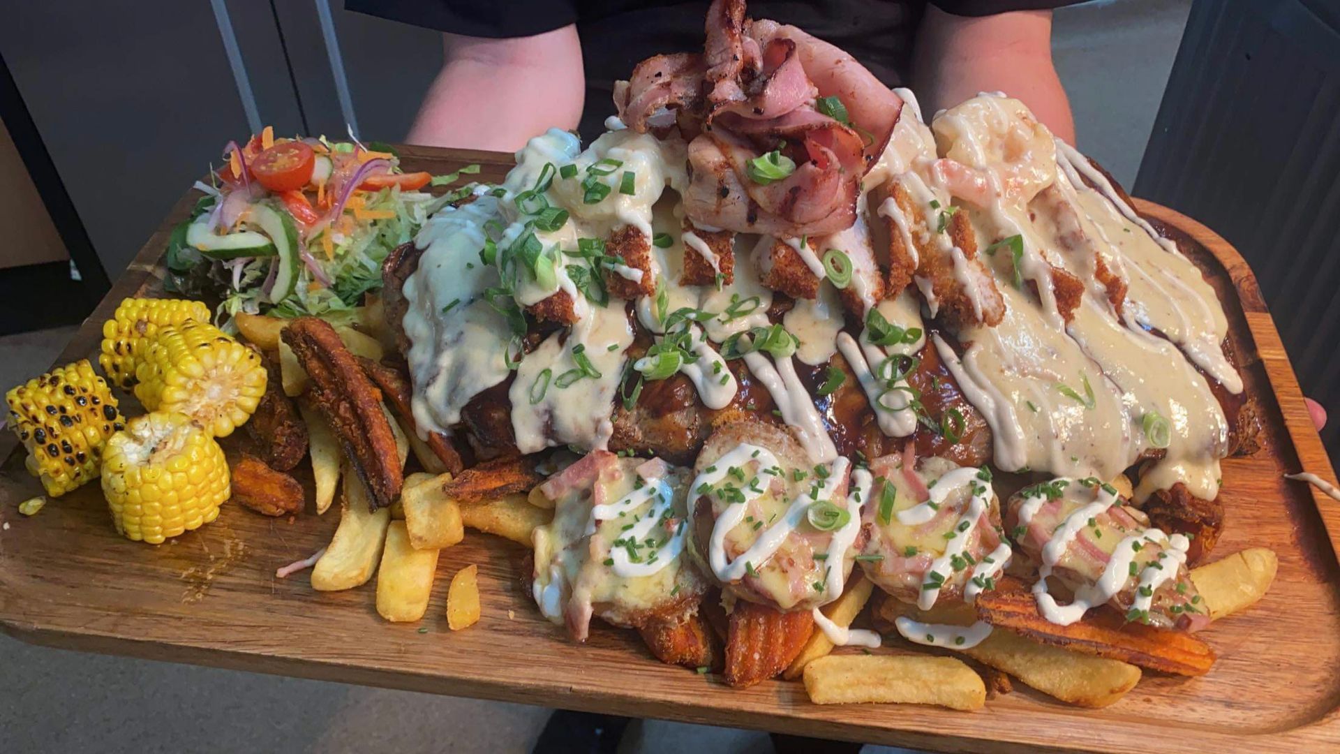 A person is holding a wooden cutting board filled with lots of food.