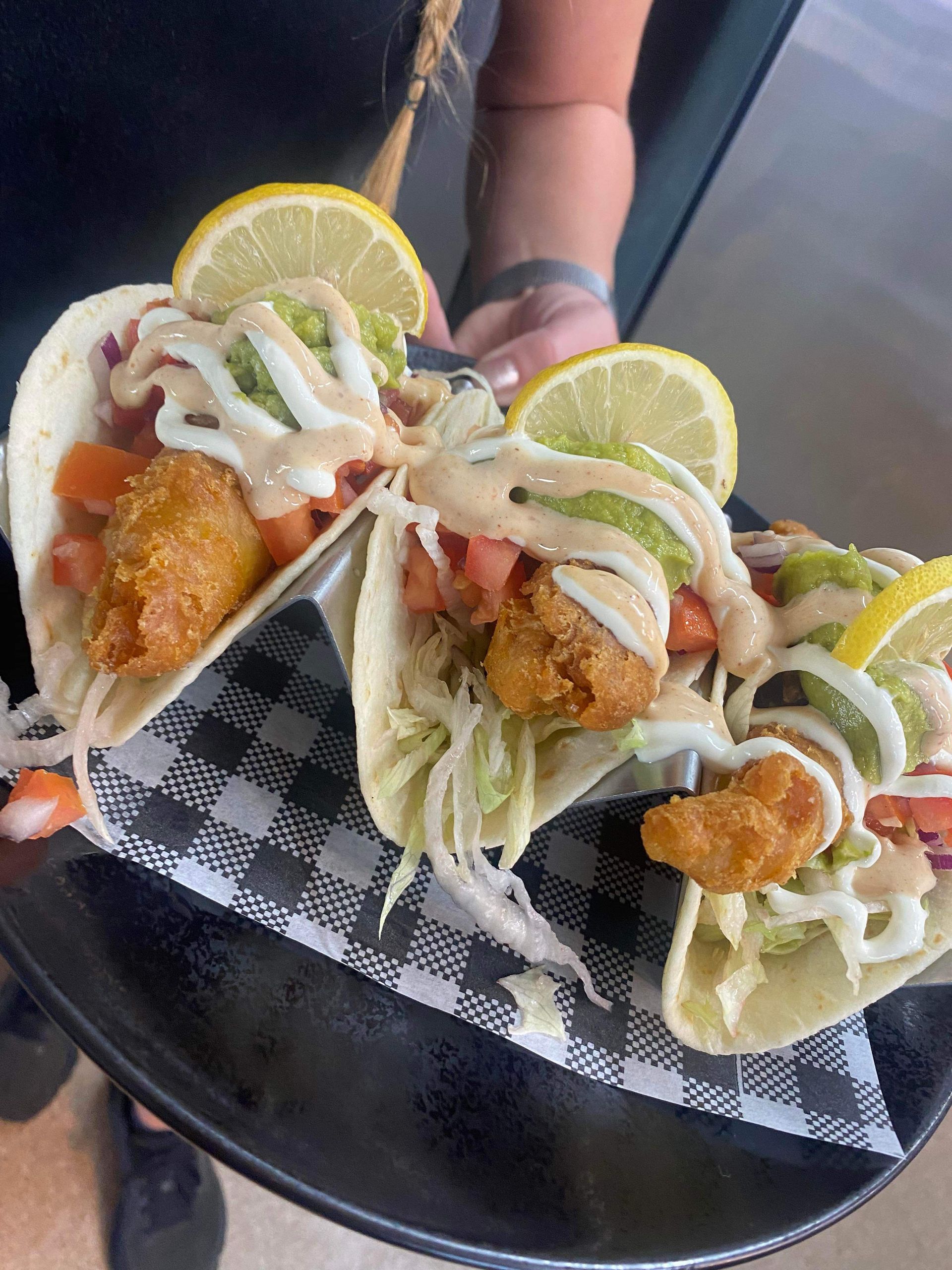 A person is holding a black plate with three tacos on it.