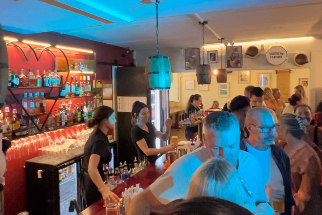 A group of people are standing around a bar.