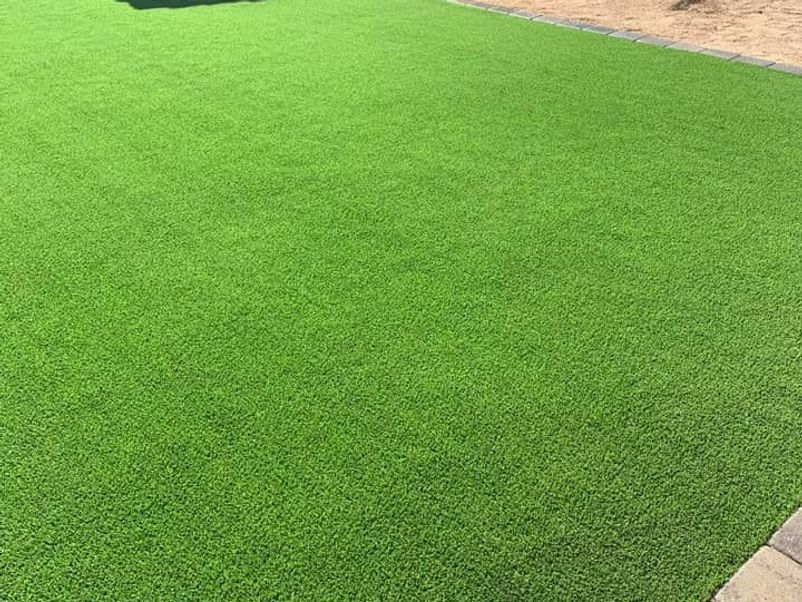Green artificial turf covers a yard with a stone border.