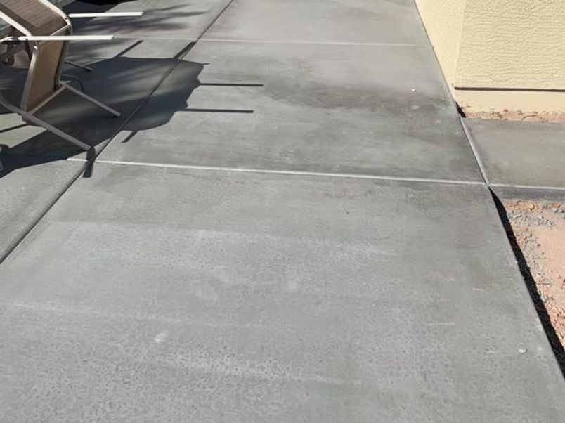 Gray concrete sidewalk with a section of an outdoor table and the side of a beige building.