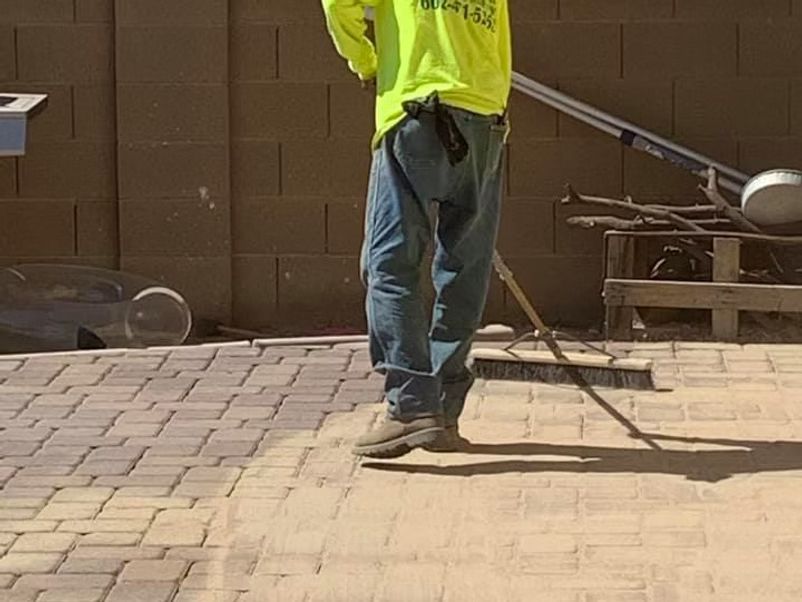 Person in a yellow shirt sweeping a brick patio with a broom.