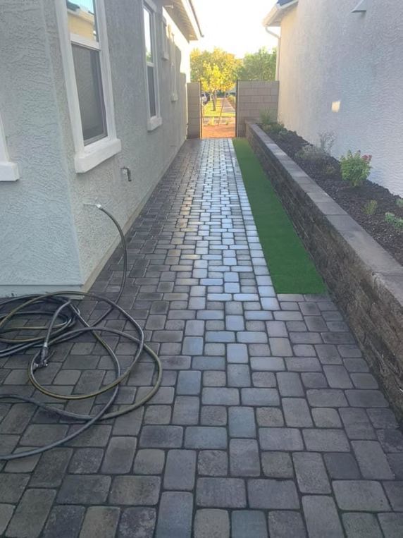Brick pathway between two buildings, with a strip of green turf and a gate at the end.