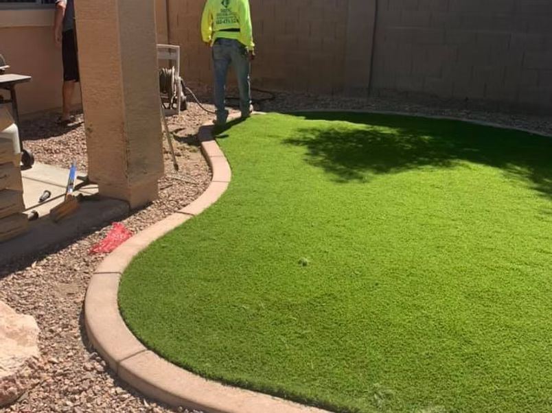 Green turf yard with curved concrete border; worker in neon vest.