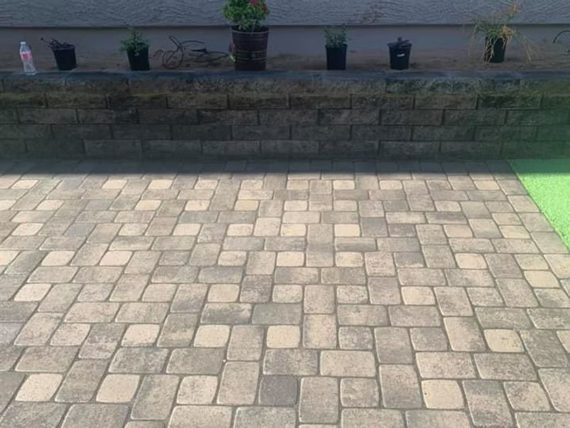 Brick patio in front of a retaining wall with potted plants.