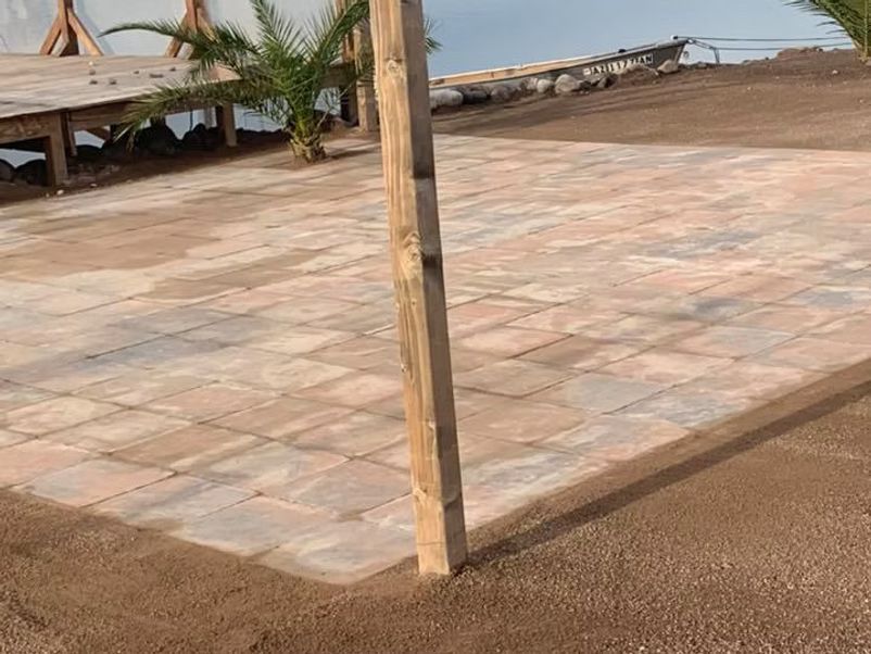 Square pavers, wooden post, beach setting with sand and a deck in the background.