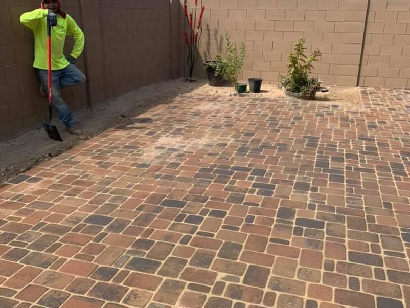 Brick patio with worker leaning on shovel against wall.