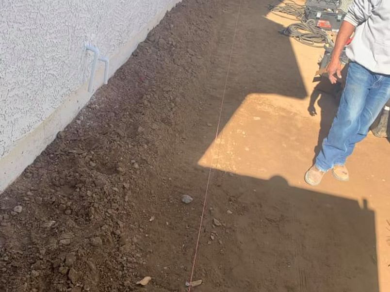 Man standing near a dirt trench next to a white wall, with string stretched across the ground.
