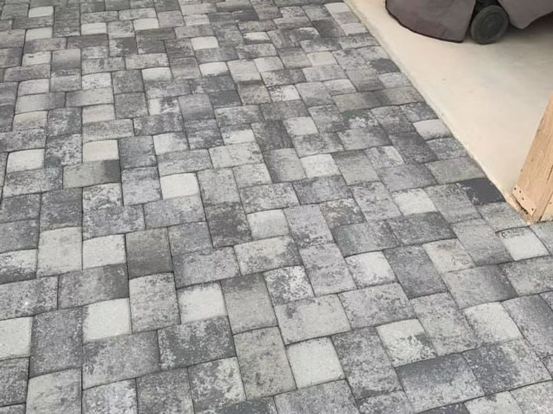 Gray and white rectangular pavers in a herringbone pattern on a patio next to a building.