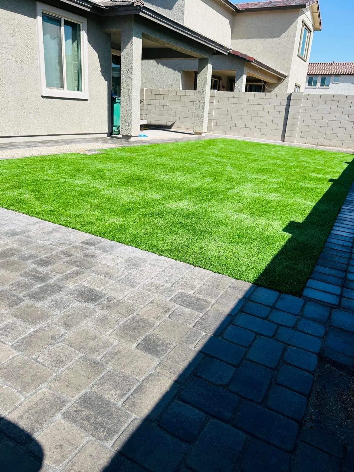 Artificial green lawn surrounded by brick pavers and a light beige house.