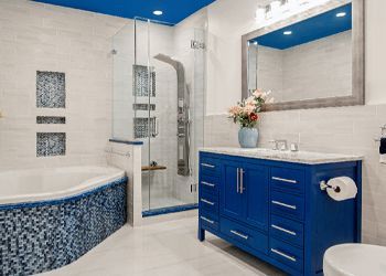 A bathroom with a blue vanity , sink , toilet and shower.
