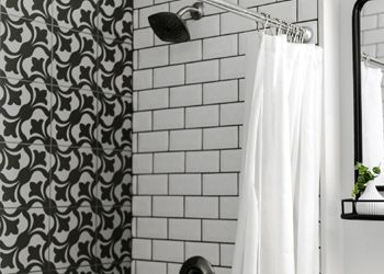 A bathroom with black and white tiles , a shower curtain , a mirror and a shower head.