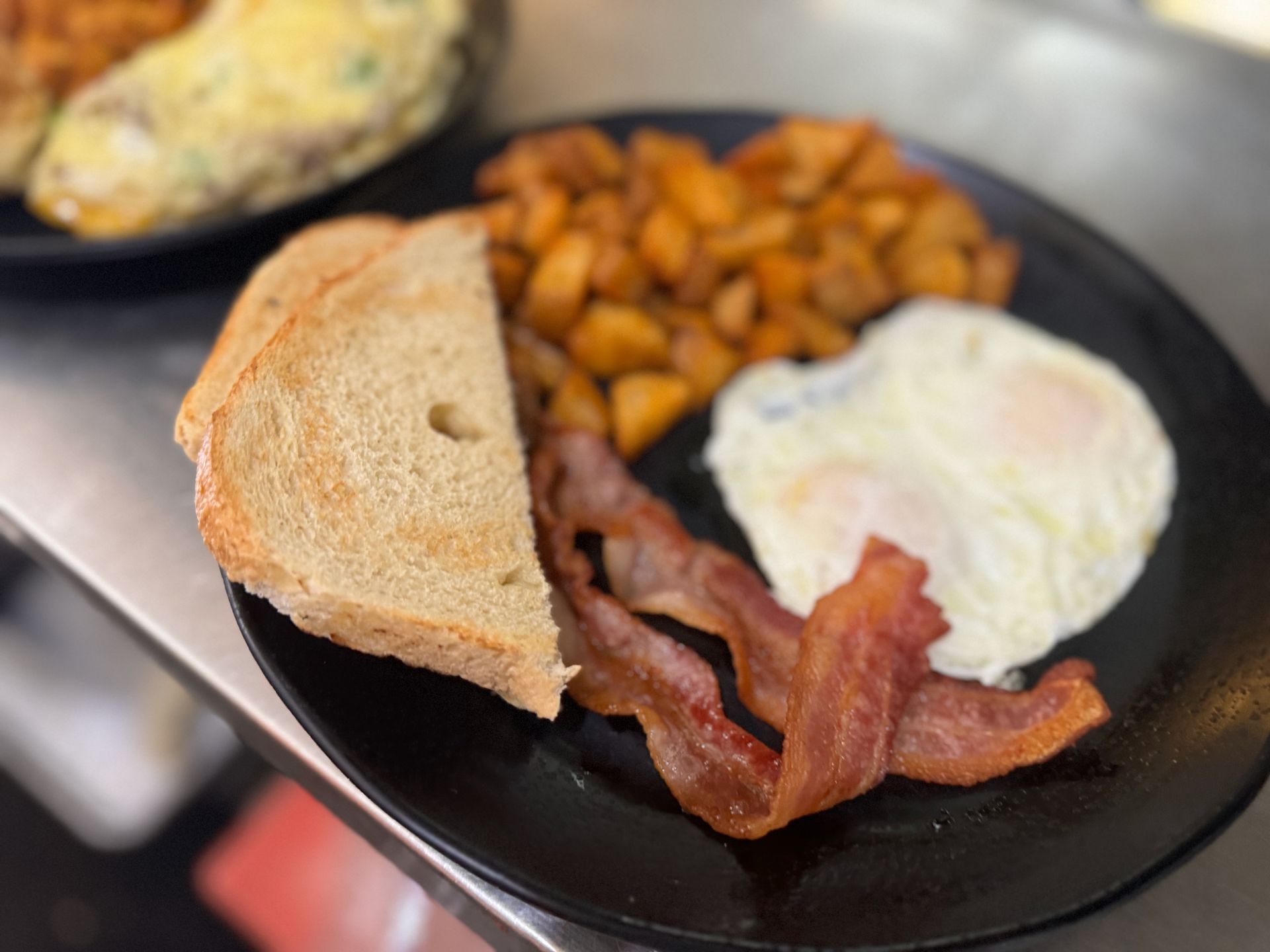 A black plate topped with eggs , bacon , toast and potatoes.