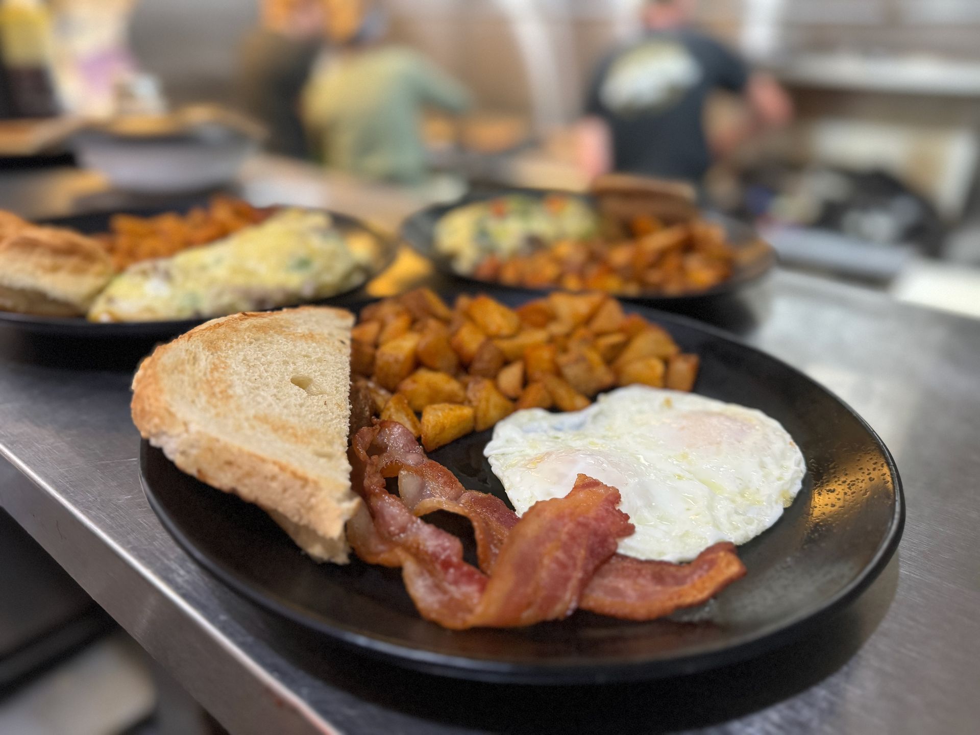 A black plate topped with eggs , bacon , potatoes and toast.