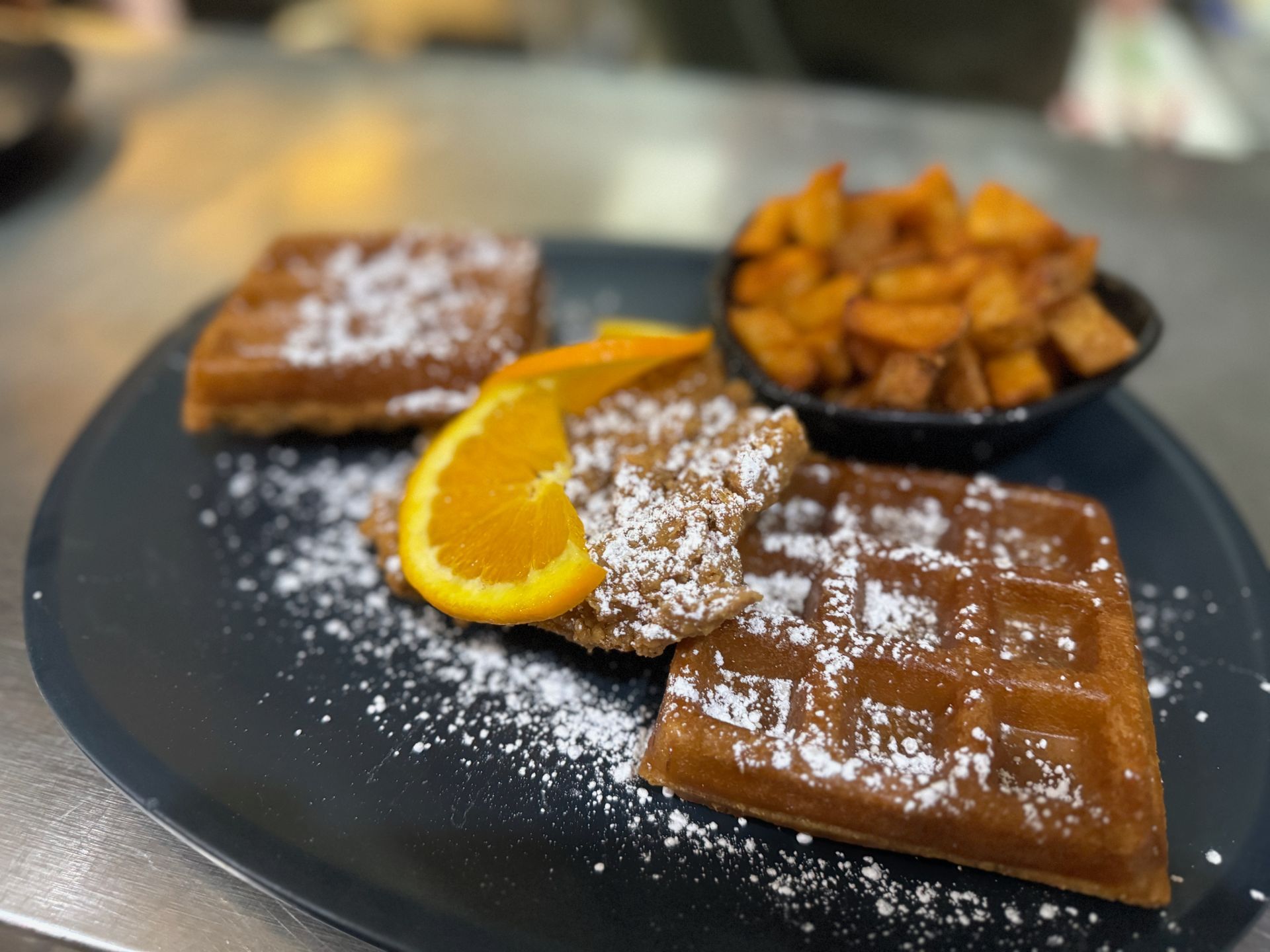 A close up of a plate of food with waffles and potatoes on a table.