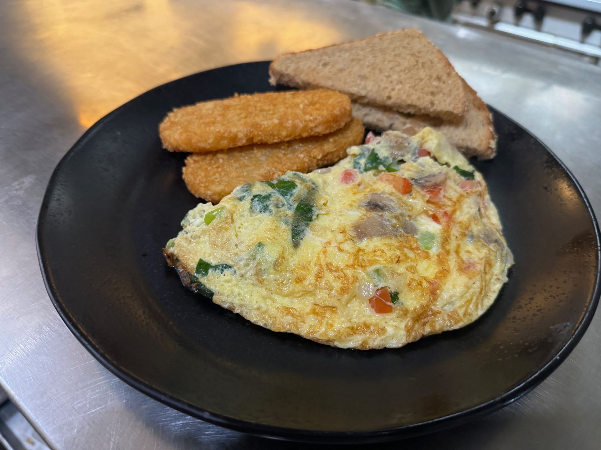 A black plate topped with an omelet , chicken nuggets and toast.