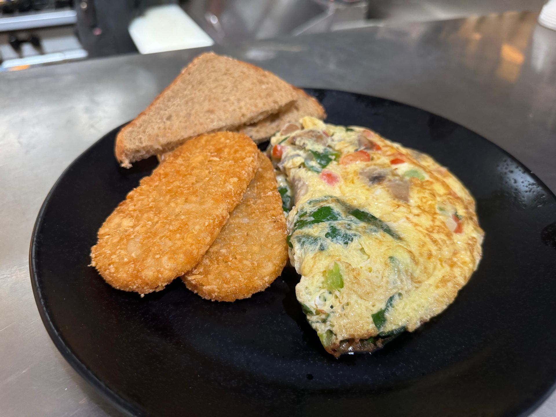 A black plate topped with an omelet , hash browns and toast.