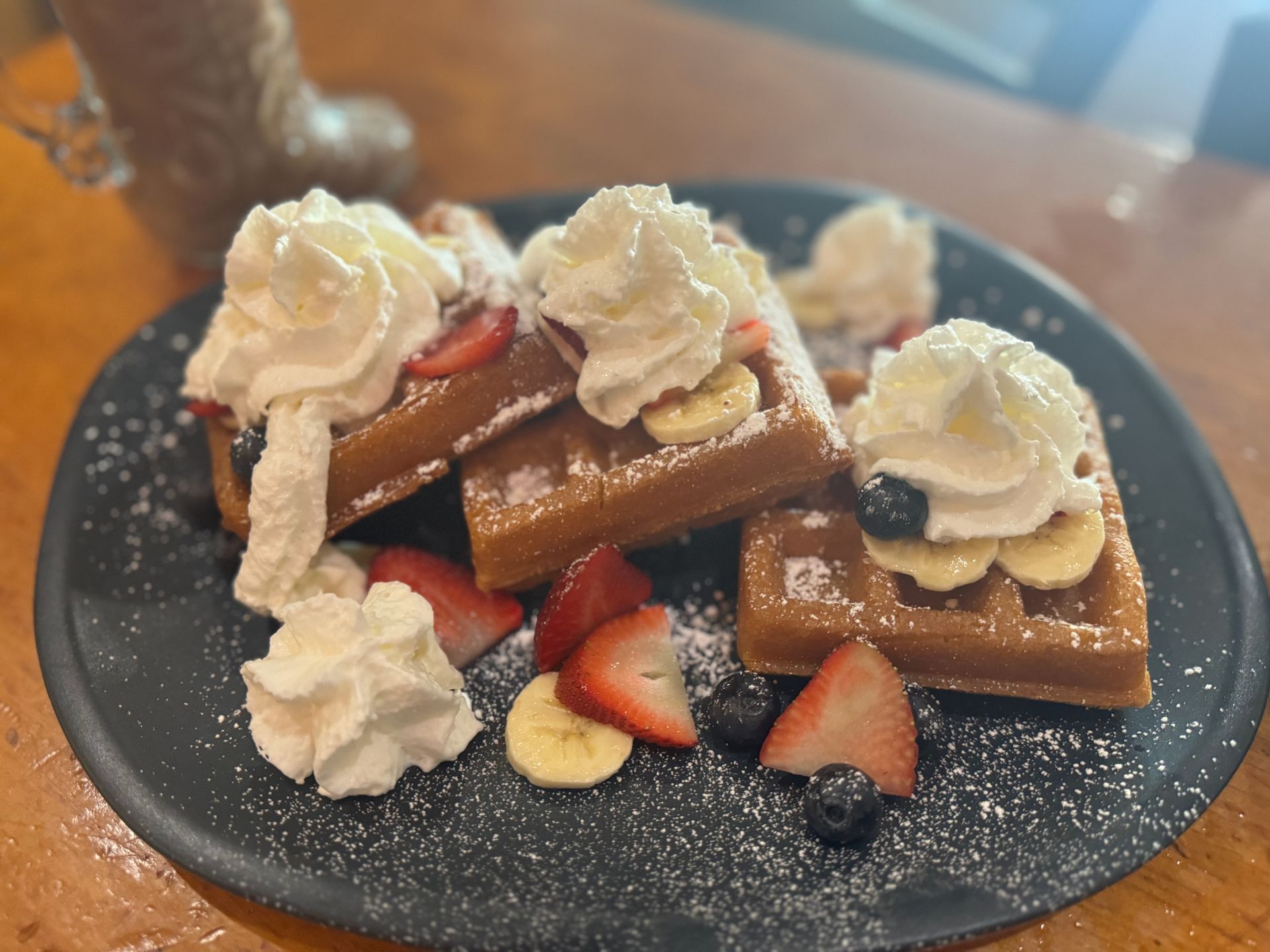 A plate of waffles with whipped cream and fruit on a table.