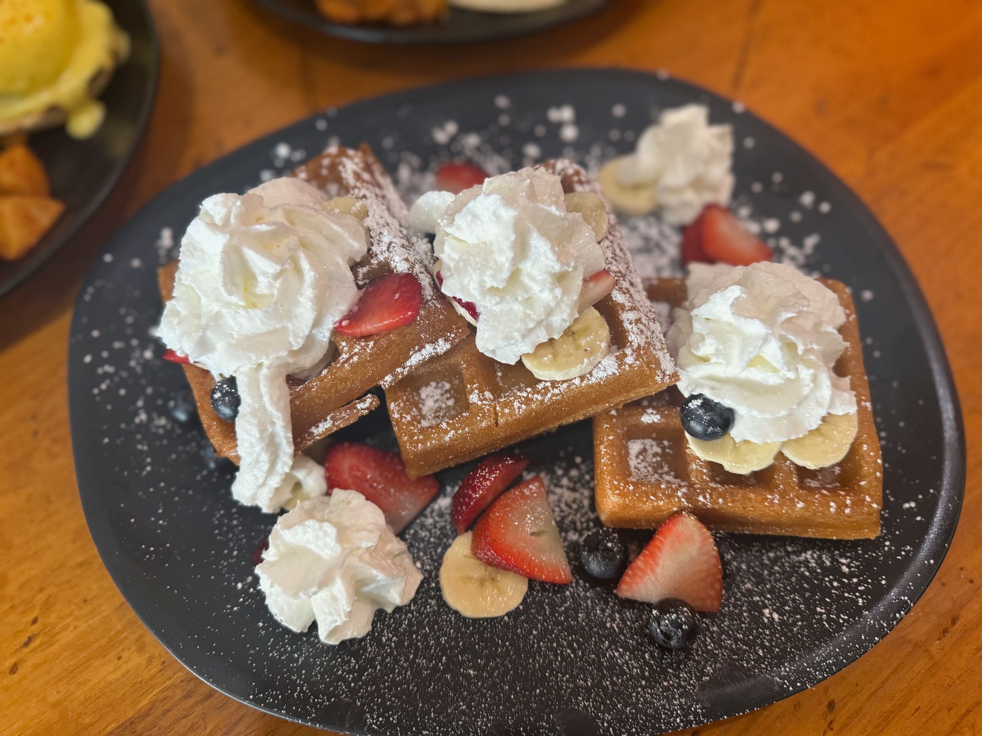 A close up of a plate of waffles with whipped cream and fruit on a table.